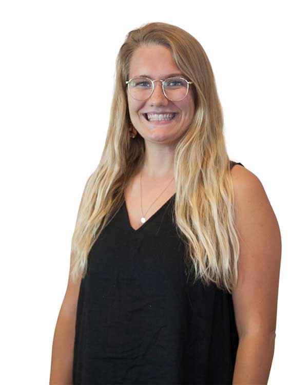 Danielle R., Office Manager at Radius Chiropractic, smiling with long hair and glasses, wearing a black top, embodying a supportive and joyful presence in the clinic.