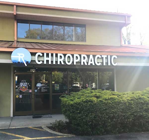 Radius Chiropractic office front in Asheville, NC, featuring a prominent sign with "CHIROPRACTIC" and a blue logo, surrounded by greenery and parking area.